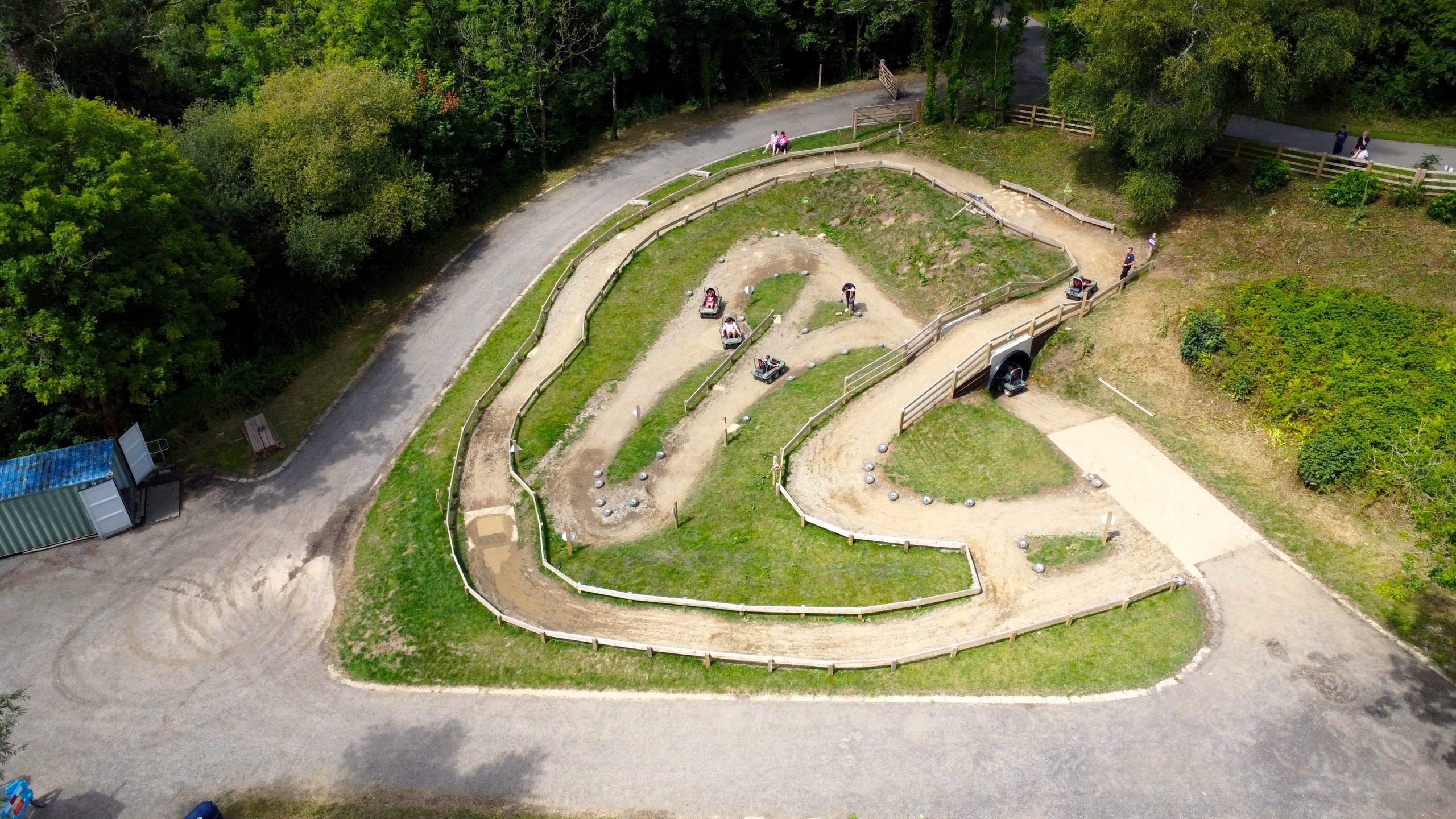 Aerial view of children driving Crazi-Bugz buggies on a winding off-road track lined with tyres and wooden fencing, set among woodland.