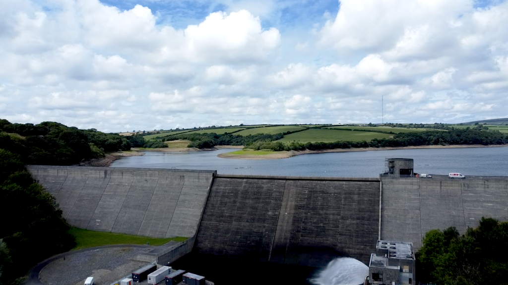 Llys-y-Frân reservoir and dam, with rolling fields and woodland under a cloudy sky.